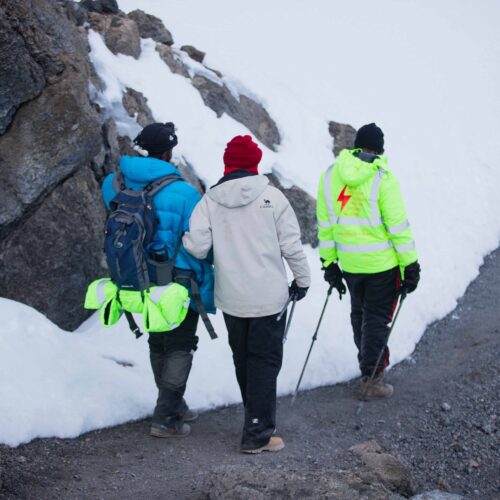 Three hikers navigate a snowy mountain trail, equipped with winter gear.